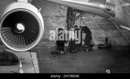 Black and white image of maintenance ground crew checking and repairing airplane chassis wheels before taking off. Stock Photo