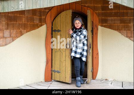 girl comes out through an ancient wooden door from a colorful playhouse Stock Photo