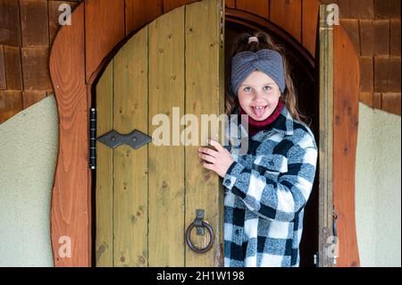 girl comes out through an ancient wooden door from a colorful playhouse Stock Photo