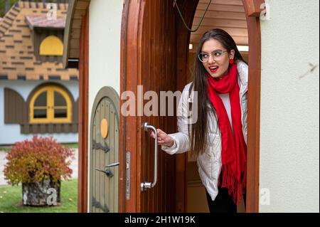 beautiful young woman in glasses carefully looking around opens an ancient wooden door and comes out Stock Photo