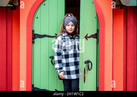 The girl comes out through the green wooden door of a colorful playhouse Stock Photo