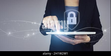 Cyber security, digital crime concept. White tablet in businesswoman hand with digital hologram lock, padlock icon sign on grey back. Data protection Stock Photo