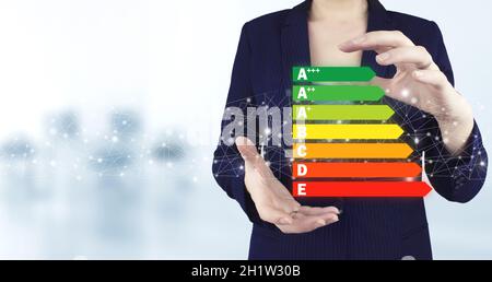 Good energy chart rating. Two hand holding virtual holographic energy efficiency icon with light blurred background. Concept of ecological and bio ene Stock Photo