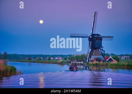 Netherlands rural lanscape with windmills at famous tourist site Kinderdijk in Holland in twilight with full moon and boat in canal Stock Photo