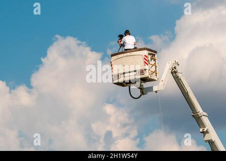 Cameraman working on an aerial work platform. The unrecognizable cameraman shoots a video, view from back. Stock Photo