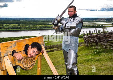 Dramatization penalty in the middle ages. Knight swung his sword at the prisoner. Knightly armor and weapon. Semi - antique photo. Stock Photo