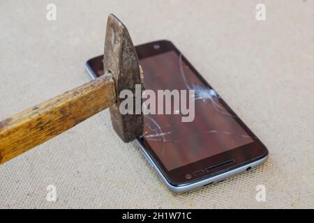 Hammer and smartphone. The screen of the smartphone, a broken hammer. The destruction of the phone. Stock Photo