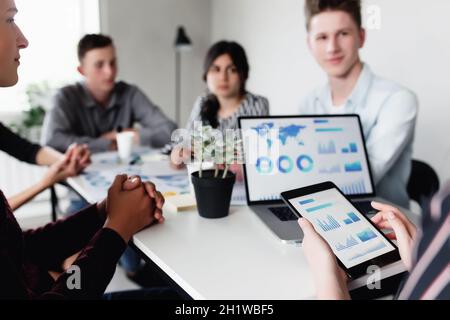 Business planning meeting, young colleagues or partners sitting together at table in conference room with graphics, charts presented by manager, discu Stock Photo