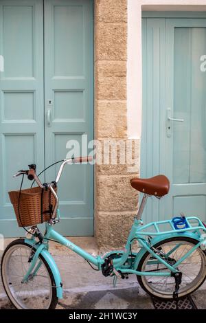 a bicycle with a wicker basket in front of the door of a house in Polignano a Mare Stock Photo