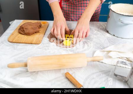 Woman's hands cut out cookies from the dough in the form of ginger man. Close-up of hands and table with kitchen utensils. The concept of home cooking Stock Photo