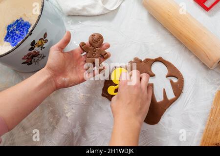 Woman's hands cut out cookies from the dough in the form of ginger man. Top view. Close-up of hands and a table with cookies. The concept of home cook Stock Photo