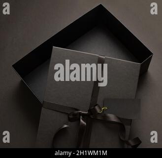 Black Friday sale concept, Gift box open cover tied with ribbon bow and empty tag on black background. Winter season holiday promotion offer Stock Photo