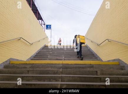 Ukraine, Kiev - September 26, 2019: A walking Glovo courier service provider with a yellow backpack rises the steps of the transition, hurries to deli Stock Photo