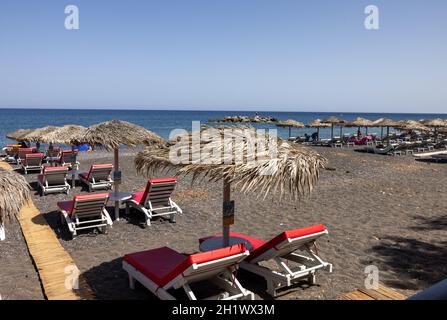 Kamari, Santorini, Greece - June 27, 2021: Sun loungers on the black volcanic beach of Kamari in Santorini. Cyclades, Greece Stock Photo