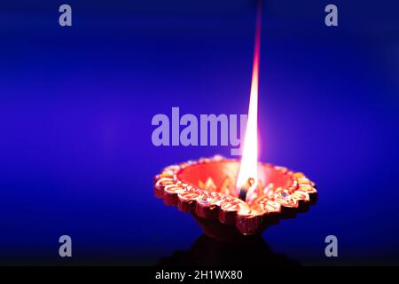 Handcrafted Eco Friendly Clay Diya Deep Dia Glowing With Flowers On Blue Background. Indian Festival Theme For Diwali Pooja, Navratri, Dussehra Puja, Stock Photo