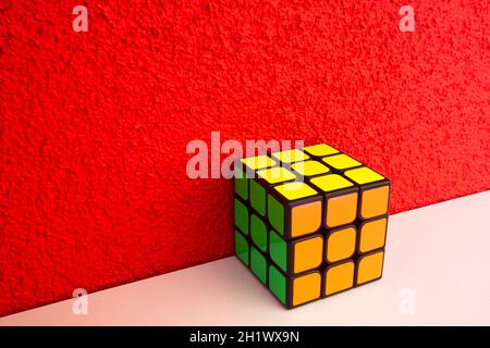 Solved puzzle speed cube on white wooden shelf near red colored wall, colorful rubiks cube with copy space mind challanging retro design Stock Photo