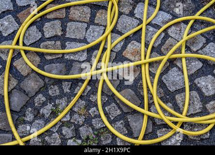 Top view of hosepipe on grass and cobblestone surfaces. Minimalistic conception. Stock Photo