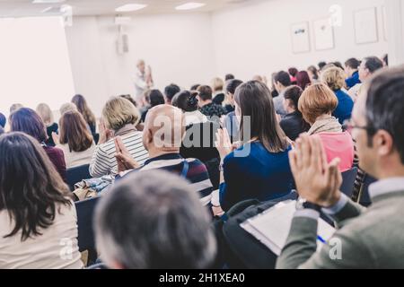 Life coaching symposium. Female speaker giving interactive motivational speech at entrepreneurship workshop. Audience in conference hall. Rear view of Stock Photo