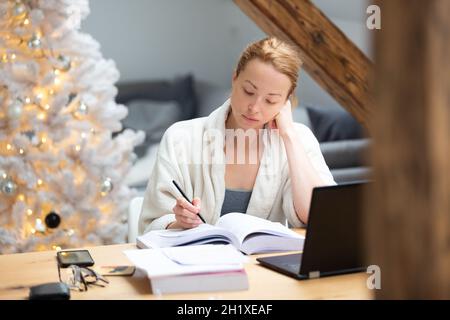 Young businesswoman wearing cosy warm bathrobe working remotly from home in winter Christmas time during 2020 corona virus pandemic. Work from home, s Stock Photo