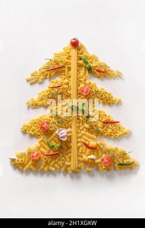 Alternative creative Christmas tree of dry different shape Italian pasta with tomatoes and basil isolated on white background. Xmas vertical greeting Stock Photo