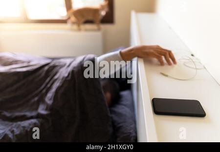 Screen addiction concept.Man who has screen or mobile addiction , trying to reach smartphone as he wakes up. Stock Photo