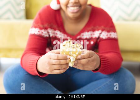 Midsection of african american plus size woman in santa hat holding present home Stock Photo