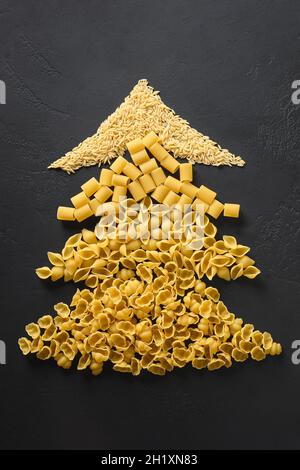 Alternative creative Christmas tree of different dry pasta on black background. Xmas greeting card. View from above. Food holiday concept. Stock Photo