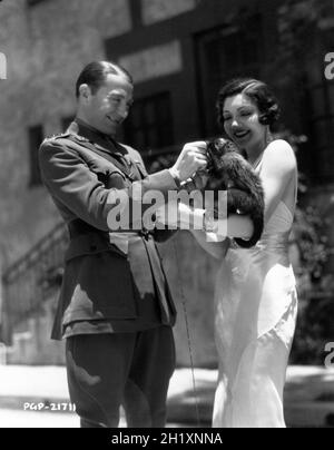 CLIVE BROOK and CLAUDETTE COLBERT on Paramount Studios Lot with Rango the studio pet monkey on set candid during a break in filming of THE MAN FROM YESTERDAY 1932 director BERTHOLD VIERTEL costume design Travis Banton Paramount Pictures Stock Photo