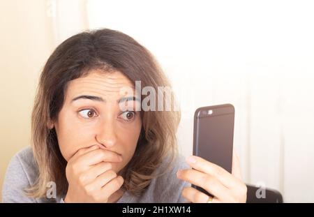 Woman looking mobile phone screen with worried eyes. Stock Photo