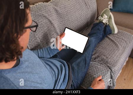Rear view of disabled man holding coffee cup using digital tablet with copy space on couch at home Stock Photo