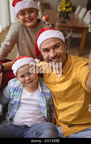 Caucasian father and two sons smiling while talking a selfie at home during christmas Stock Photo