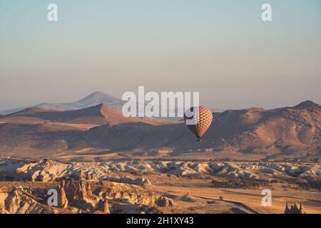landscape with lonely hot air balloon with checkered pattern rising over the Cappadocian valley panorama in the morning light