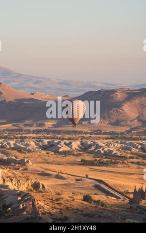 landscape with lonely hot air balloon with checkered pattern rising over the Cappadocian valley panorama in the morning light