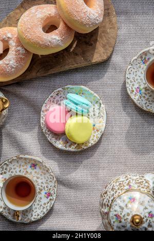 Cup of tea and macarons on diner table, antique tea pot set and doughnuts for afternoon tea top view Stock Photo