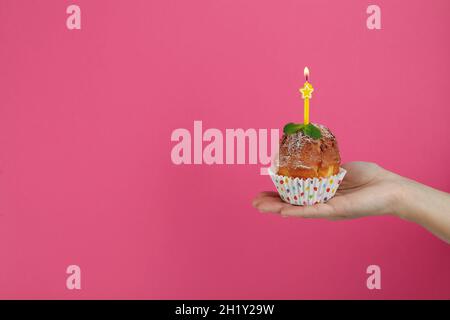 Female hand holds muffin with one candle on pink background. Stock Photo