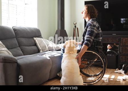 Caucasian disabled man with dog sitting on wheelchair looking out of the window at home Stock Photo