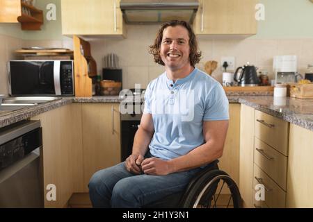 Portrait of caucasian disabled man sitting on wheelchair smiling in the kitchen at home Stock Photo