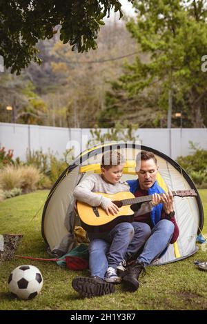 Caucasian father and son playing guitar together while sitting in a tent in the garden Stock Photo