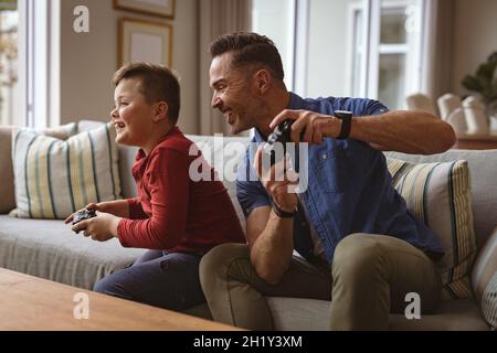 Caucasian father and son playing video games together sitting on the couch at home Stock Photo
