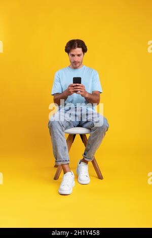 Focused guy using cellphone at studio, sitting on chair Stock Photo