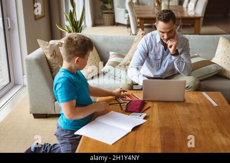 Caucasian father using laptop while son doing his homework at home Stock Photo
