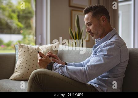 Caucasian man using smartphone sitting on the couch at home Stock Photo