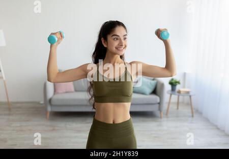 Portrait of beautiful young Indian woman keeping fit, training with dumbbells at home. Staying healthy during lockdown Stock Photo