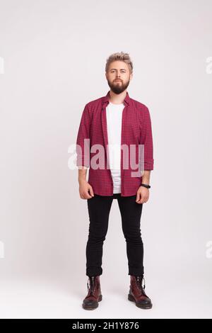 Full length body of serious self-confident man with beard wearing stylish plaid shirt and casual black pants standing straight, looking at camera. Indoor studio shot isolated on gray background Stock Photo