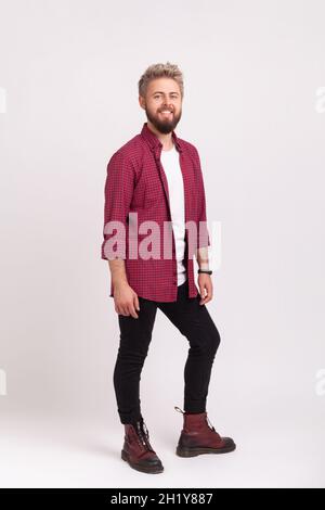 Full length body of happy bearded man in stylish plaid shirt and casual black pants smiling looking at camera, hipster male rejoicing. Indoor studio shot isolated on gray background Stock Photo