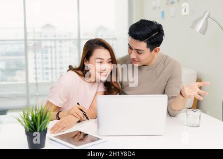 Positive hipster couple having fun while working together remotely at home using modern technology Stock Photo