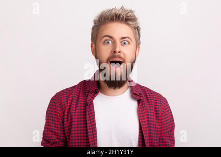 Portrait of extremely surprised caucasian bearded man looking at camera with open mouth and big eyes, happy satisfied with good cashback. Indoor studio shot isolated on gray background Stock Photo