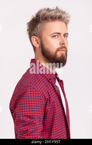 Side view portrait of handsome concentrated bearded young adult man in plaid t-shirt thoughtfully looking to side. Indoor studio shot isolated on gray background Stock Photo