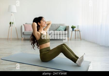 Fit Indian woman exercising on yoga mat, strengthening abs muscles at home, full length Stock Photo