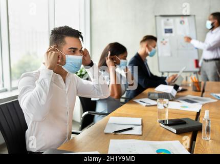 Diverse Multiethnic Colleagues Putting On Medical Masks During Corporate Meeting In Office Stock Photo